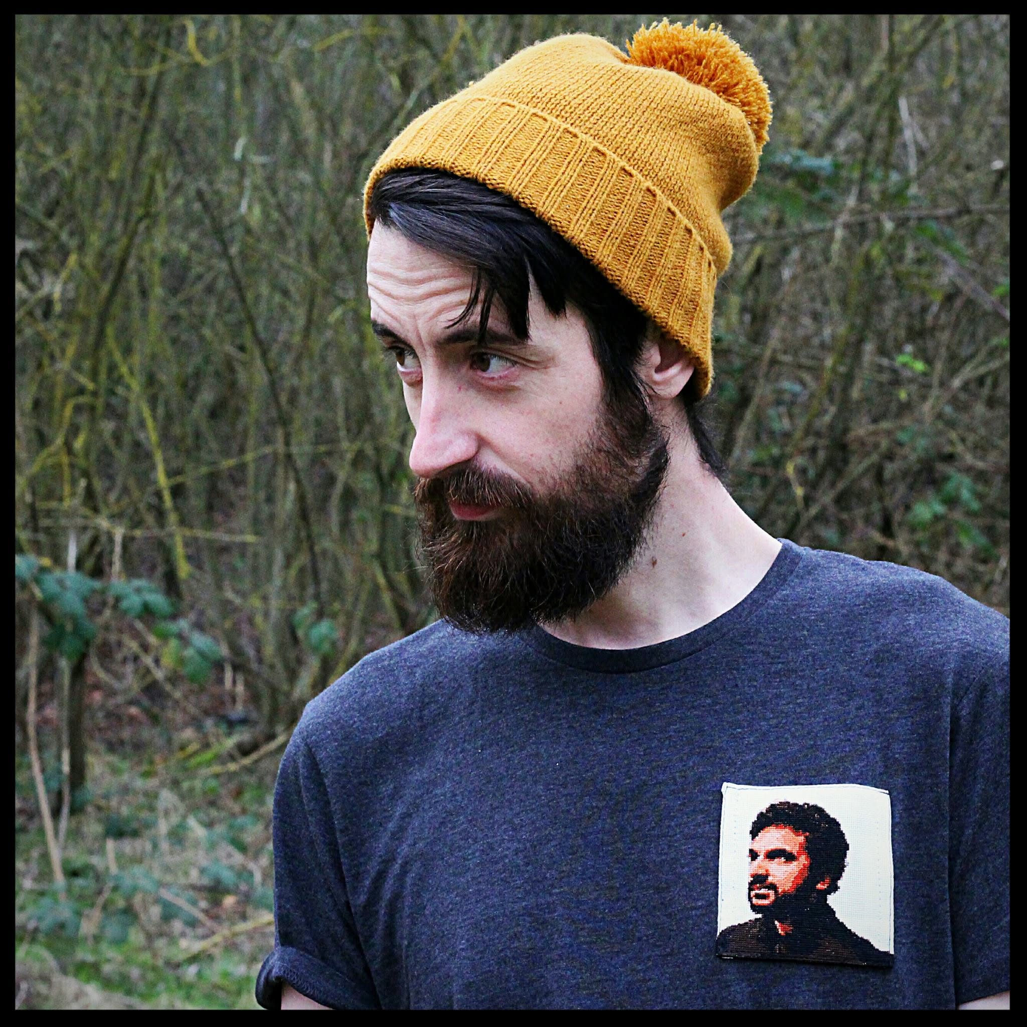 A cross-stitch of Nish Kumar, attached as a patch pocket to a t-shirt.